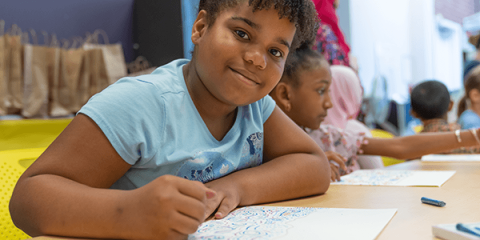 Young girl in blue shirt drawing at a table.