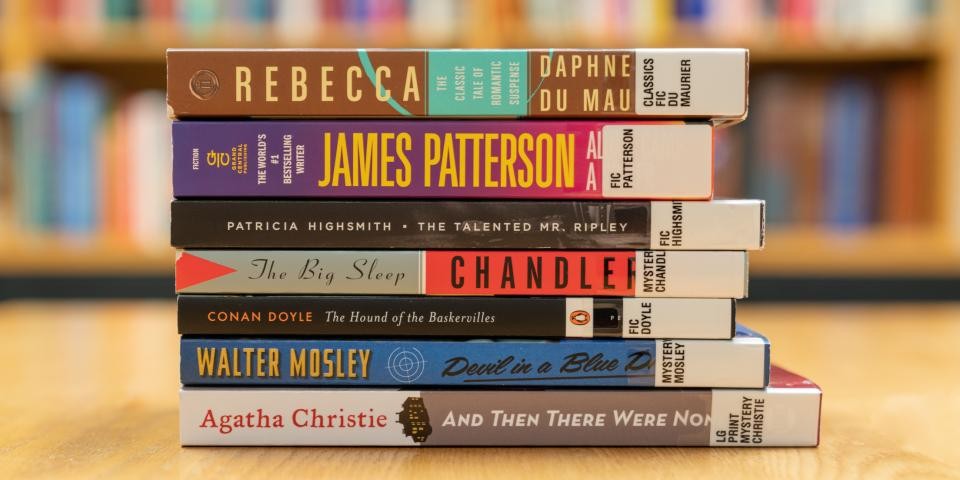 Stack of books on a wooden desk, with bookshelves in the background.