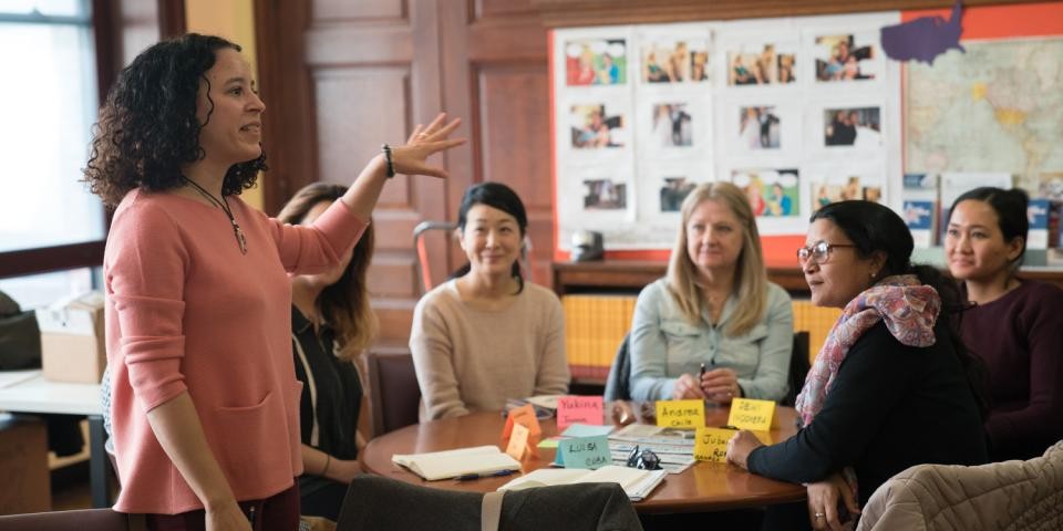 adults sit around a circular table listening to a teacher