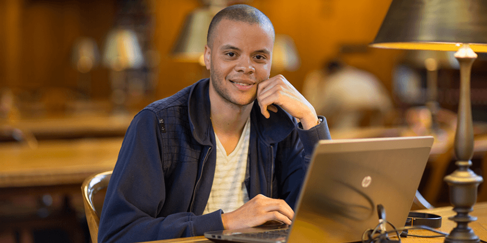 A researcher sits at a table in the Rose Main Reading Room with an open laptop.