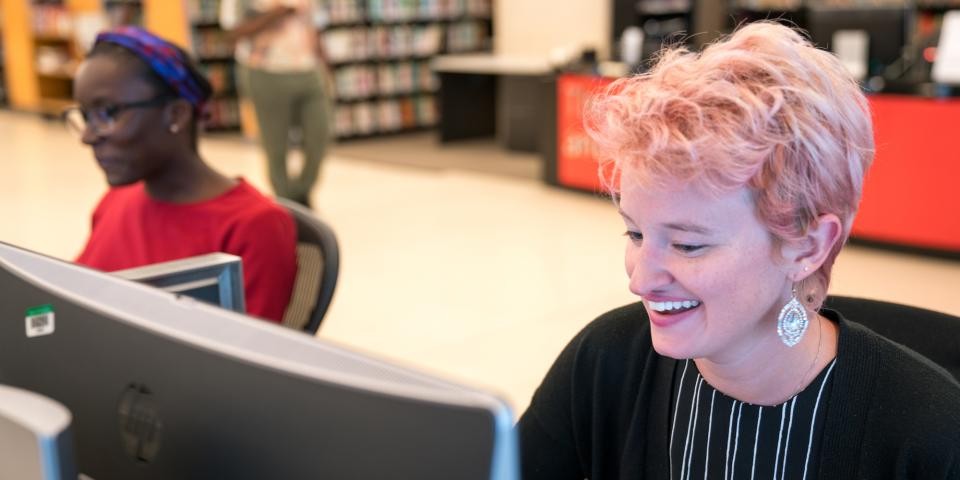 Two people sit at computers inside the Library for the Performing Arts.