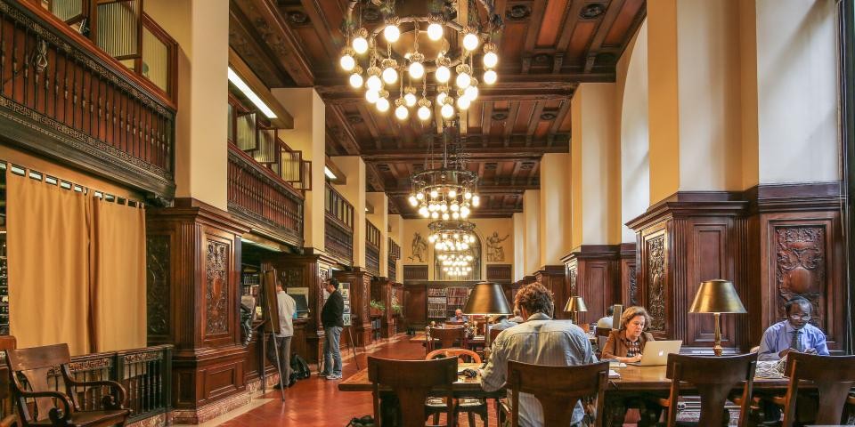 Interior the Dorot Jewish Division, featuring rich wood details, chandeliers, and researchers in various parts of the room. 