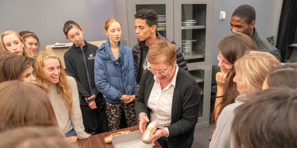 A class gathers around a researcher who is holding up a ballet slipper.