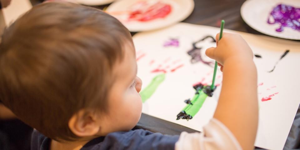 A small child with short brown hair paints an abstract picture.