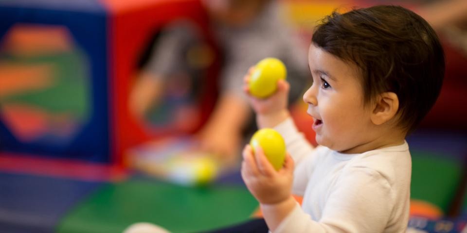 A small child with short black hair and a white shirt holds two yellow egg-shaped toys.