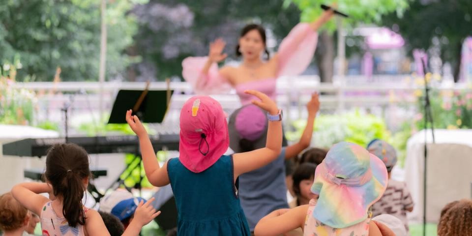 A group of children with their arms into the air watch a performer in front of them on stage.