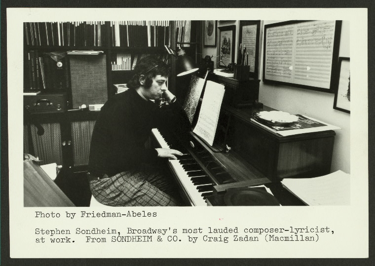 A black and white archival image of Stephen Sondheim sitting a piano in his office.