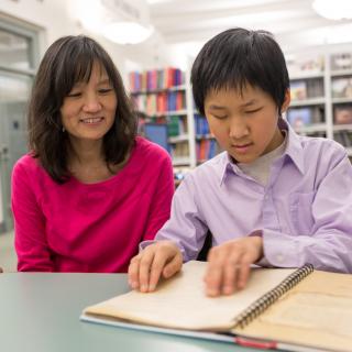 Woman watches young patron reading Braille