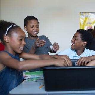 Photo of three children smiling while participating in a hands-on science program featuring paper machê