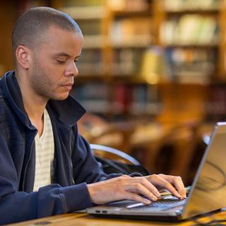 A library patron sits at a table while typing on a laptop.