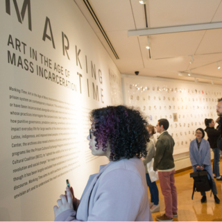 People are looking at a wall which has artwork. 