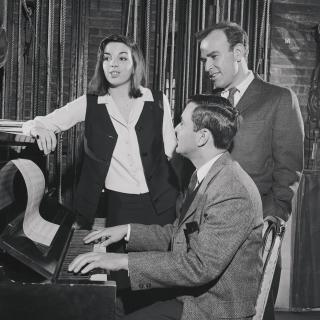 three people sit around a piano