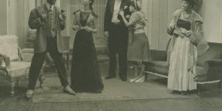 Five actors stand next to one another on a domestic stage set wearing 1940s clothing