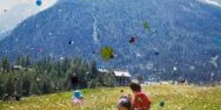 a photograph of two people in a sunlit meadow ,with a mountain range looming in the bacground is dotted with drops of paint. The bright colors are faded and look almost part of the scene; so drops of color seems to float down from the sky on the subjects.  