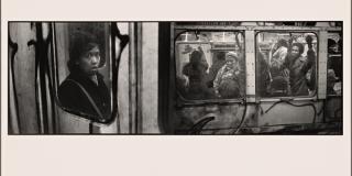 Black and white photograph of a woman looking towards the camera from inside the subway cart