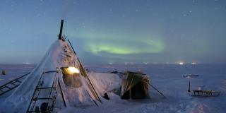 Image of a tent covered in snow, with the northern lights in the background