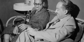 Black and white photo of two men seated, Langston Hughes and Dizzy Gillespie holding a trumpet