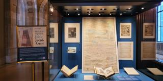 Photograph of a display case filled with books, maps, and manuscripts against a blue background