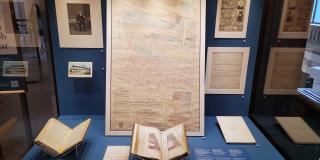 Photograph of books, manuscripts, prints, and a large map arranged in a display case against a blue background