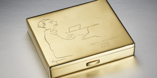 A gold cigarette case featuring a man sitting at a piano