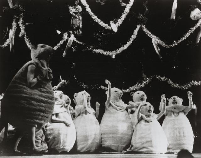 A black and white photo of several mice kneeling in front of a Christmas tree. A larger mouse is standing to the left.