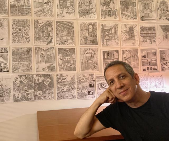 Peter Kuper sits in front of a wall displaying his drawings