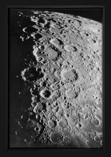 Black-and-white transparency showing a close-up of a portion of the moons cratered surface, its horizon curving in the upper right corner of the image