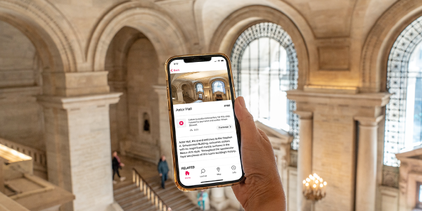 Hand holding a phone with the audio tour in the white marble Astor Hall