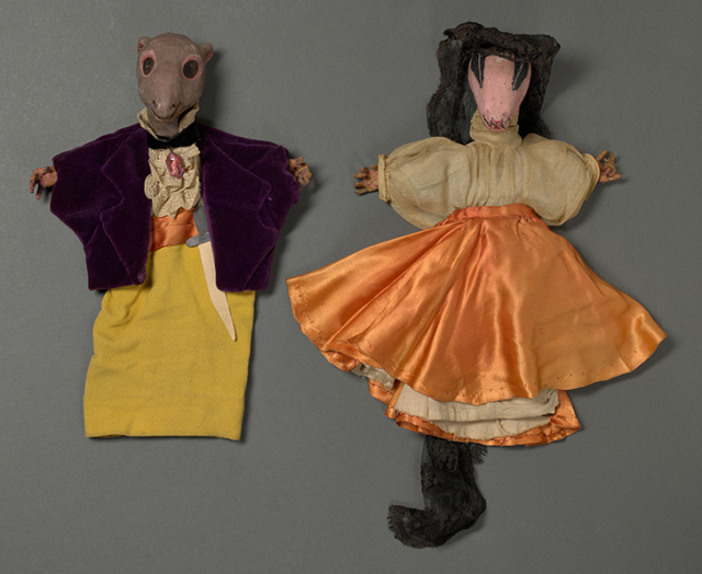 Two hand puppets with painted faces and hands, a mouse wearing a shirt and velvet coat and a cockroach wearing a veil, blouse, and dress.