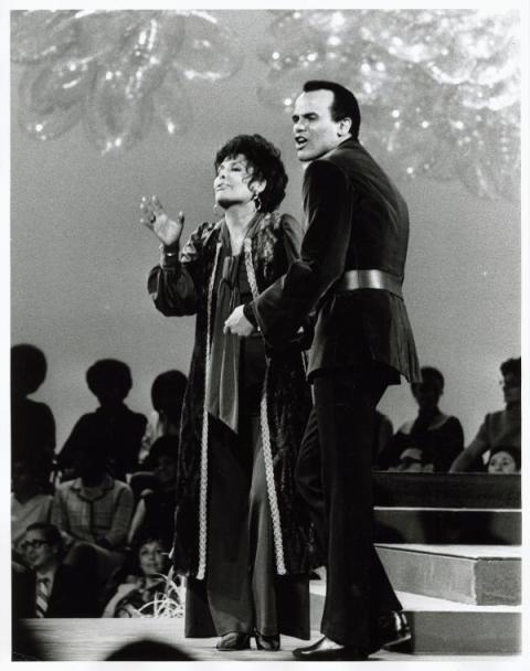 Harry Belafonte stands in fitted suit next to Lena Horne on a stepped stage. 