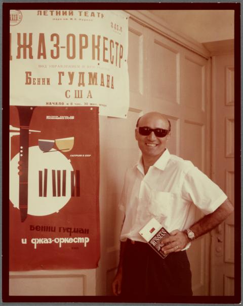 George Avakian is shown smiling with shades on next to a concert poster