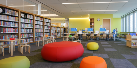 Interior photo of Charleston Library's Children's Room, which features bookshelves, wooden tables and chairs, and large colorful poufs. 