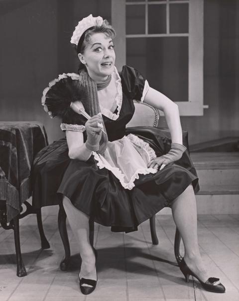 A black and white archival photo of a woman dressed in a French maid.