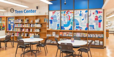 Soundview Library Teen Center, featuring a colorful mural, shelves of books and magazines lining the walls, and tables with chairs.