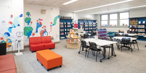 West Farms Library Teen Center, featuring red and orange furniture, a colorful wall mural, work stations, a jumbo Connect Four game, and books.