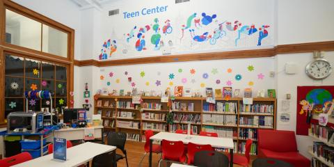 Interior of the West New Brighton Library Teen Center, featuring bookshelves, work tables, a 3-D printer, and a colorful wall mural.