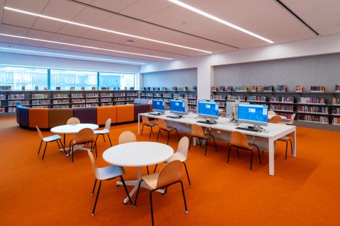 Interior of Inwood Library, featuring tables and chairs, a computer lab, and bookshelves.