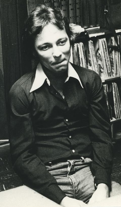 black and white photo of Blades sitting on the floor and leaning against a bookcase.